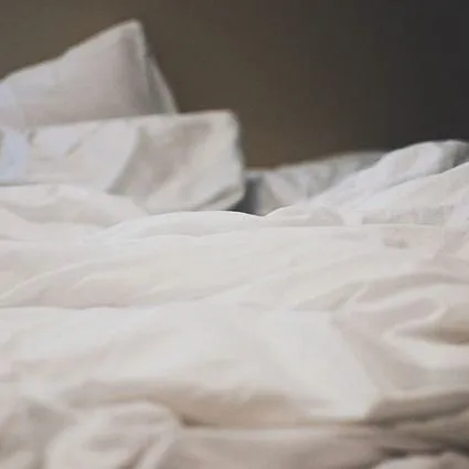 Close-up of rumpled white bed sheets and pillows on a bed.